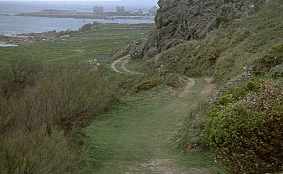 Two English Girls (1971) movie still: establishing — A dirt trail winds along a rugged, grassy cliff edge overlooking a rocky coastline. Distant…