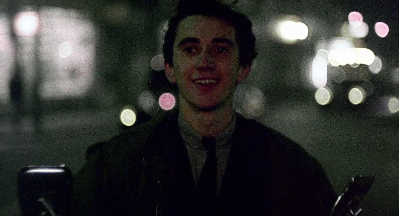 Quadrophenia (1979) movie still: medium — A dark urban environment at night with soft out-of-focus city lights in the background. A young man with…
