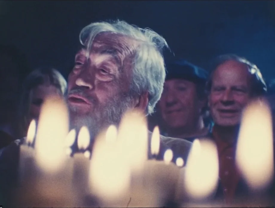 The Other Side of the Wind (2018) movie still: medium — A group of people gathers in a dark interior space illuminated by lit candles. An elderly…