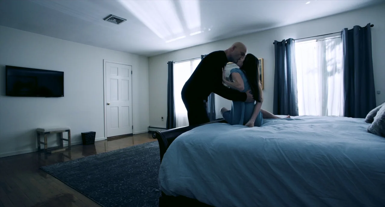 Brawl in Cell Block 99 (2017) movie still: medium — A sparely furnished room with white walls and dark hardwood floors under a rug. A bald man and a…