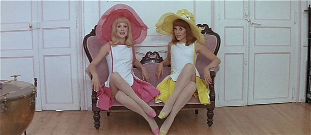 Les Demoiselles de Rochefort (1967) movie still: medium — An interior space features white paneled walls and light-colored hardwood flooring. Two…
