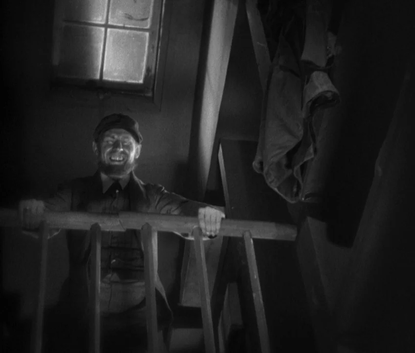 The Threepenny Opera (1931) movie still: medium — A dimly lit narrow wooden stairwell with a small frosted window above. A man stands at the top of…