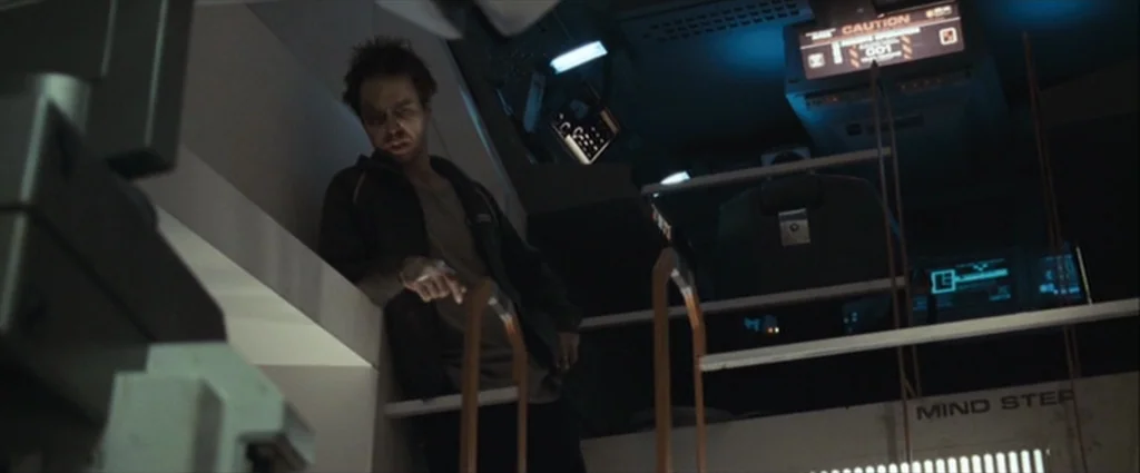 Moon (2009) movie still: medium — A dark, cramped technological environment filled with computer terminals and metal structural components. A…