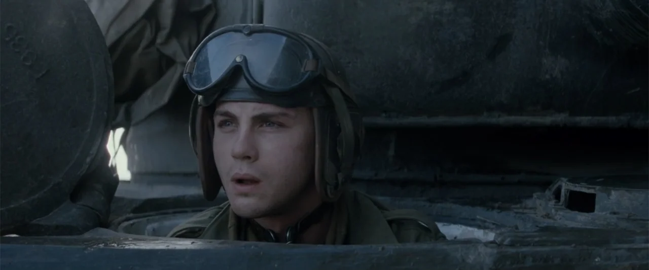 Fury (2014) movie still: closeup — A soldier in uniform stands inside the circular opening of a metal tank hatch. He looks outward with a focused…