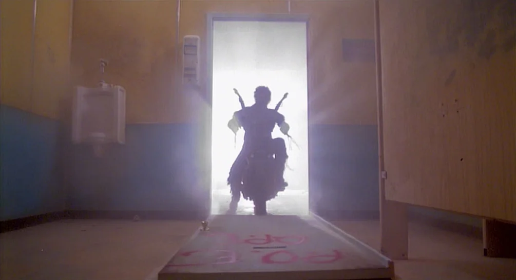 Raising Arizona (1987) movie still: fullbody — A public restroom with wood partitions and blue wall panels shows a detached door on the floor. A man…