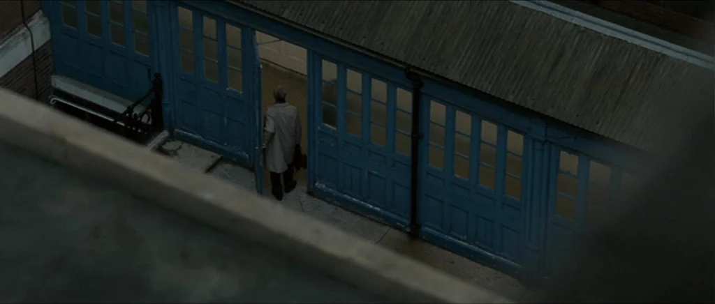 Tinker Tailor Soldier Spy (2011) movie still: wide — An exterior courtyard features a row of faded blue wooden doors under a roof. An elderly man in…