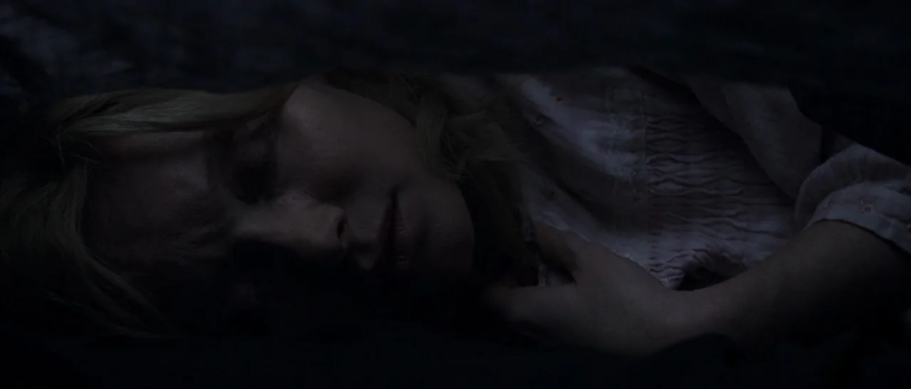 The Babadook (2014) movie still: closeup — A dark space beneath a blanket where a person rests. A woman with blonde hair sleeps with her face…