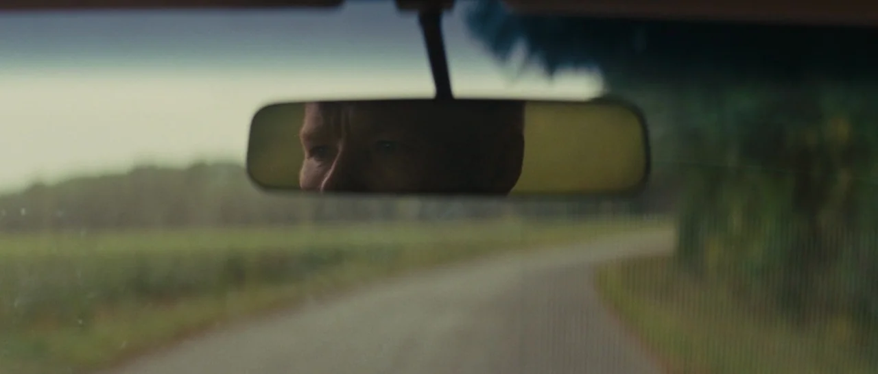 Loving (2016) movie still: closeup — The interior of a moving vehicle shows an open road visible through the windshield. A man is visible only as a…