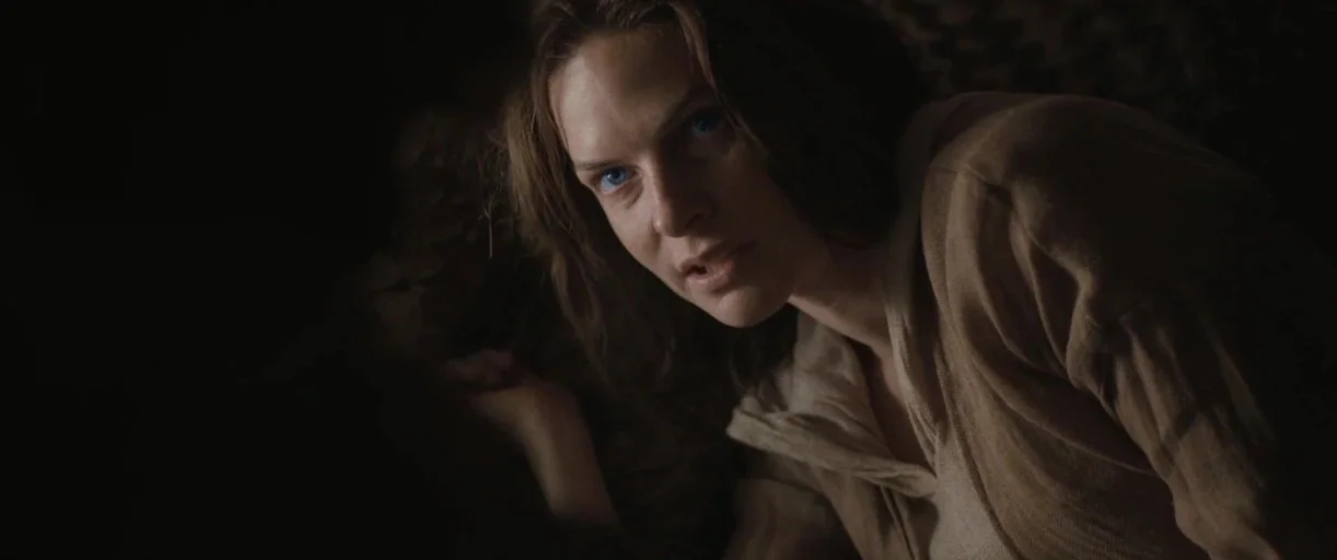 Dune: Part 2 (2024) movie still: closeup — A dark space with indistinct features and deep shadows surrounding the main subject. A woman looks upward…