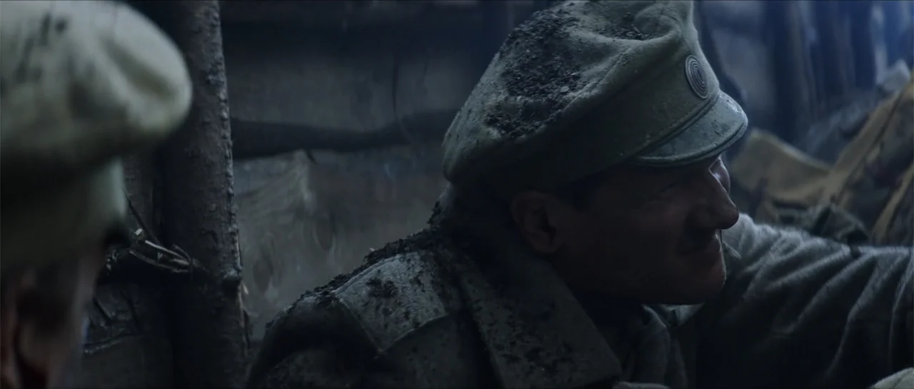 The Rifleman (2019) movie still: medium — A cramped earth-walled trench features muddy surfaces and exposed wooden support beams. A soldier wearing…