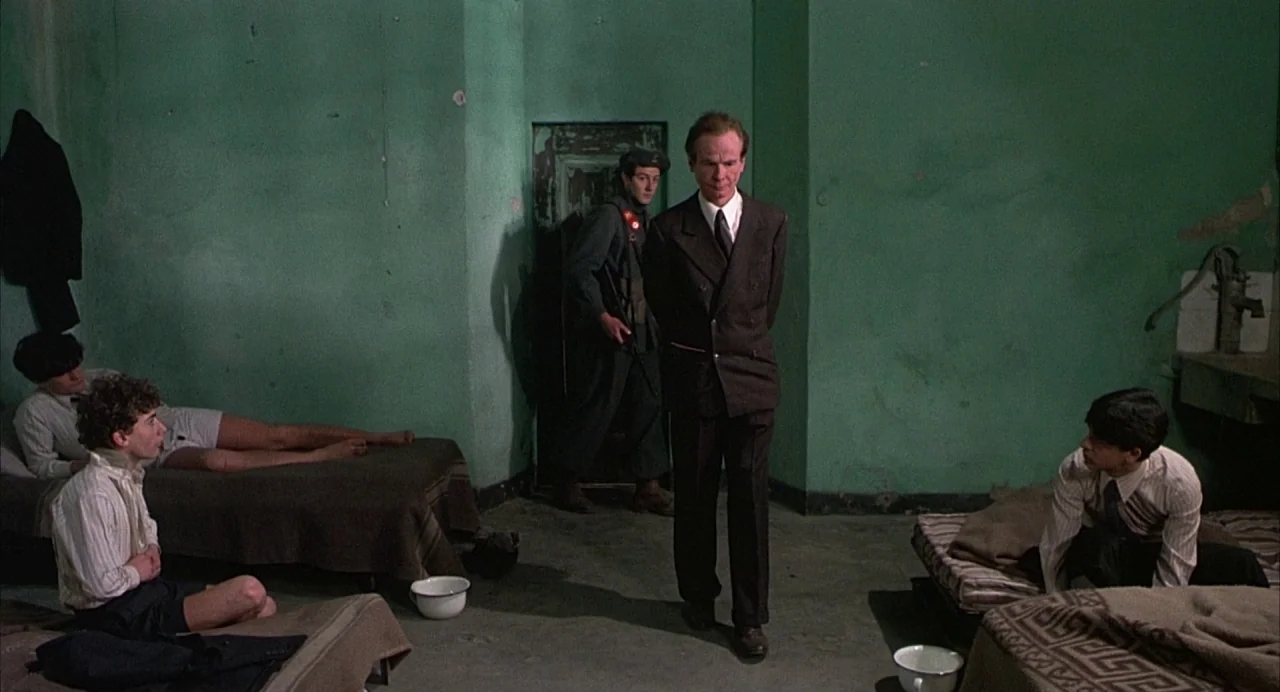 Salò, or the 120 Days of Sodom (1975) movie still: wide — A austere, green-walled institutional space contains several simple cots and one standing…