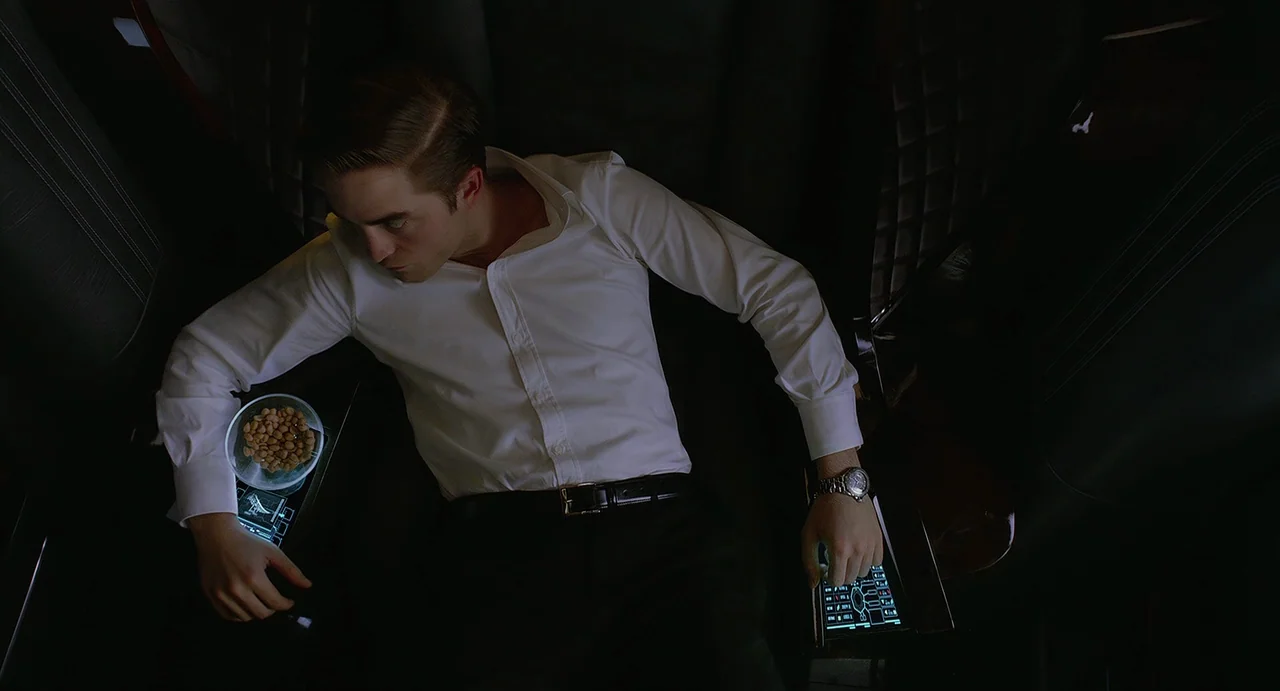 Cosmopolis (2012) movie still: medium — The interior of a luxury limousine features dark quilted leather seats and integrated touchscreens. A man…