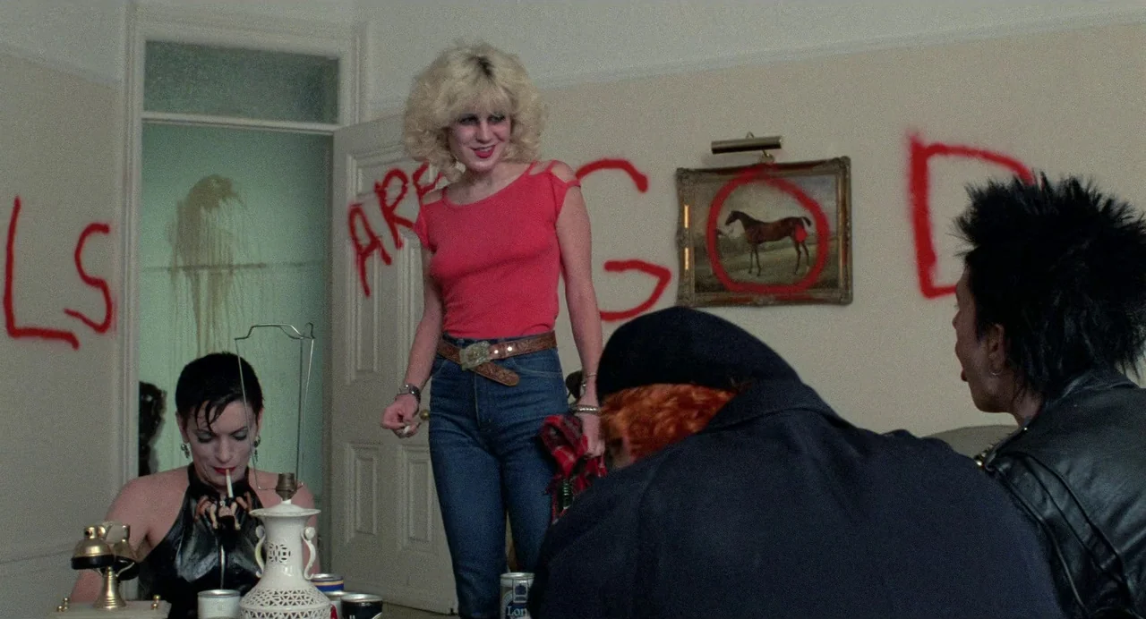 Sid and Nancy (1986) movie still: medium — A cramped apartment room features off-white walls defaced with bright red graffiti. Three people sit and…