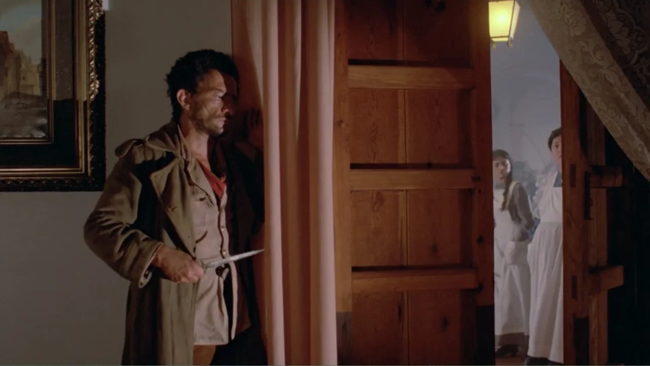 Toña Machetes (1985) movie still: medium — An interior hallway features a partially opened wooden door and heavy curtains near a frame. A man…
