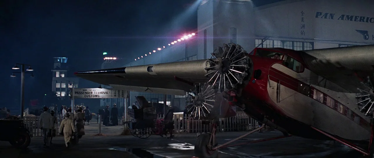 Indiana Jones and the Temple of Doom (1984) movie still: wide — A night scene at a 1930s airport with a red-and-silver trimotor aircraft parked…