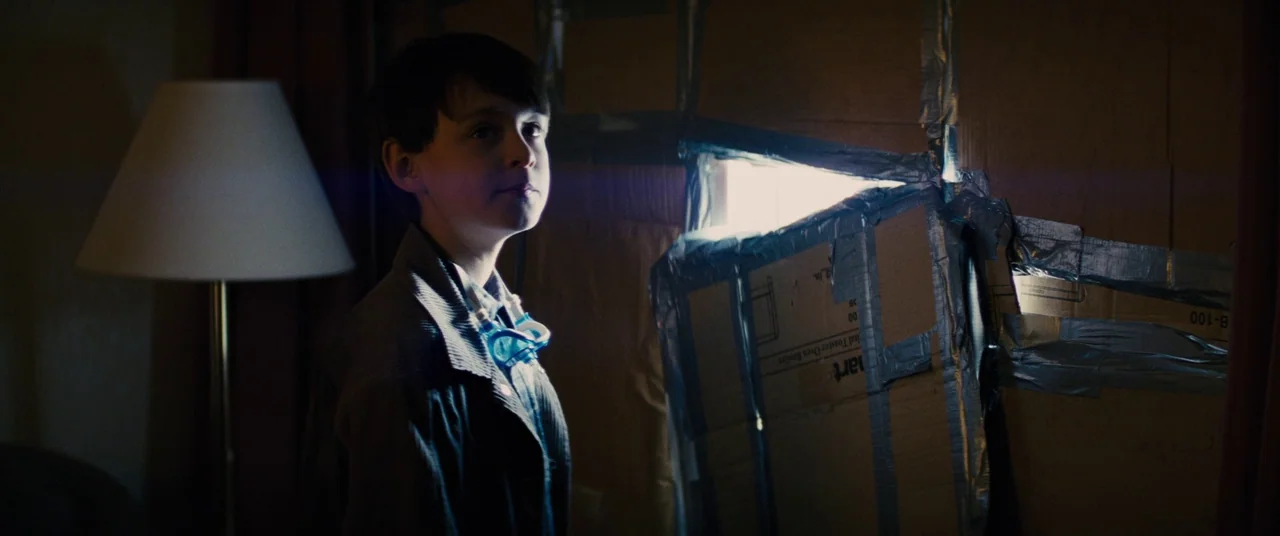 Midnight Special (2016) movie still: medium — A dimly lit room is covered in cardboard panels secured with grey duct tape. A young boy stands facing…