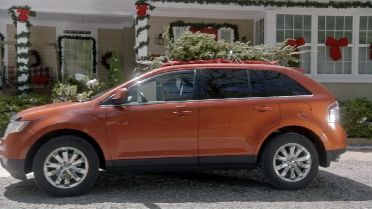 The Christmas Cure (2017) movie still: medium — An orange crossover vehicle sits in a gravel driveway before a holiday-decorated house exterior. A…