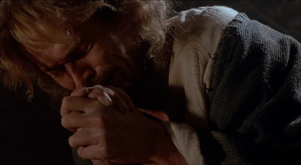 The Last Temptation Of Christ (1988) movie still: closeup — A dark, dimly lit environment with rugged, stone-like wall textures behind the subject.…
