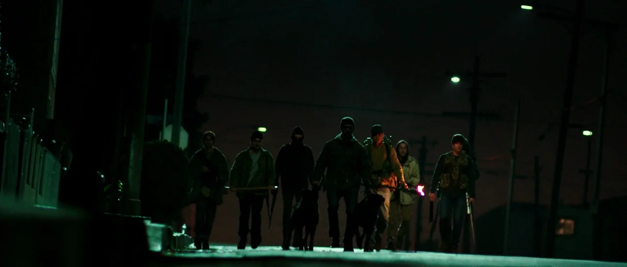 The Purge: Anarchy (2014) movie still: fullbody — A dark residential neighborhood road at night is illuminated by green-tinted municipal street…