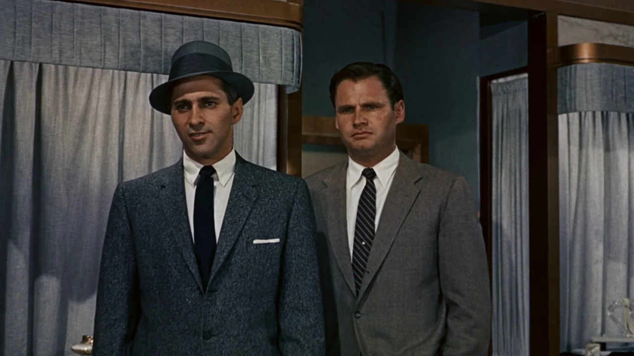 North By Northwest (1959) movie still: medium — A dressing room area with light blue curtains and modern 1950s architectural frames. Two men in…