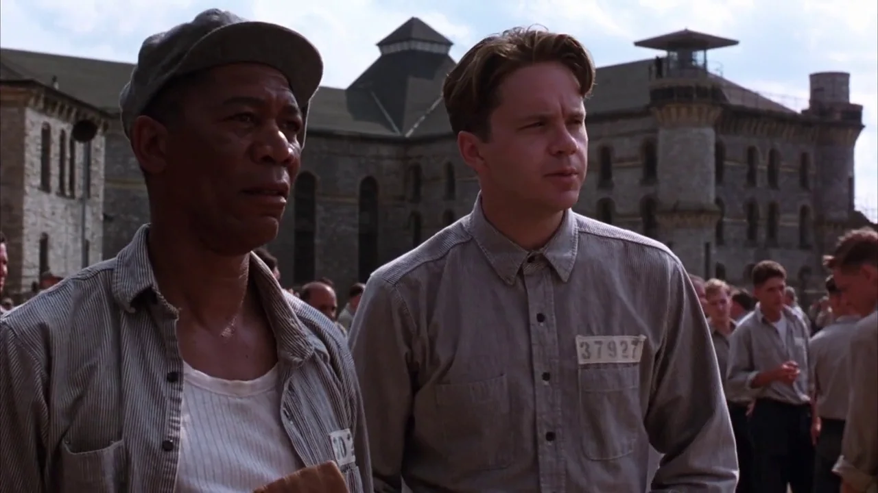 The Shawshank Redemption (1994) movie still: medium — A stone masonry facility building stands in the background of an outdoor yard area. Two men…