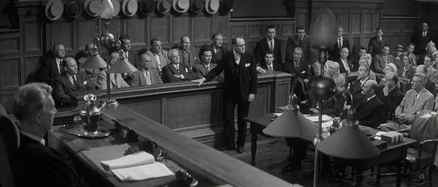 Compulsion (1959) movie still: wide — A crowded 1950s courtroom features wood-paneled walls and rows of jurors in hats. A lawyer stands near the…