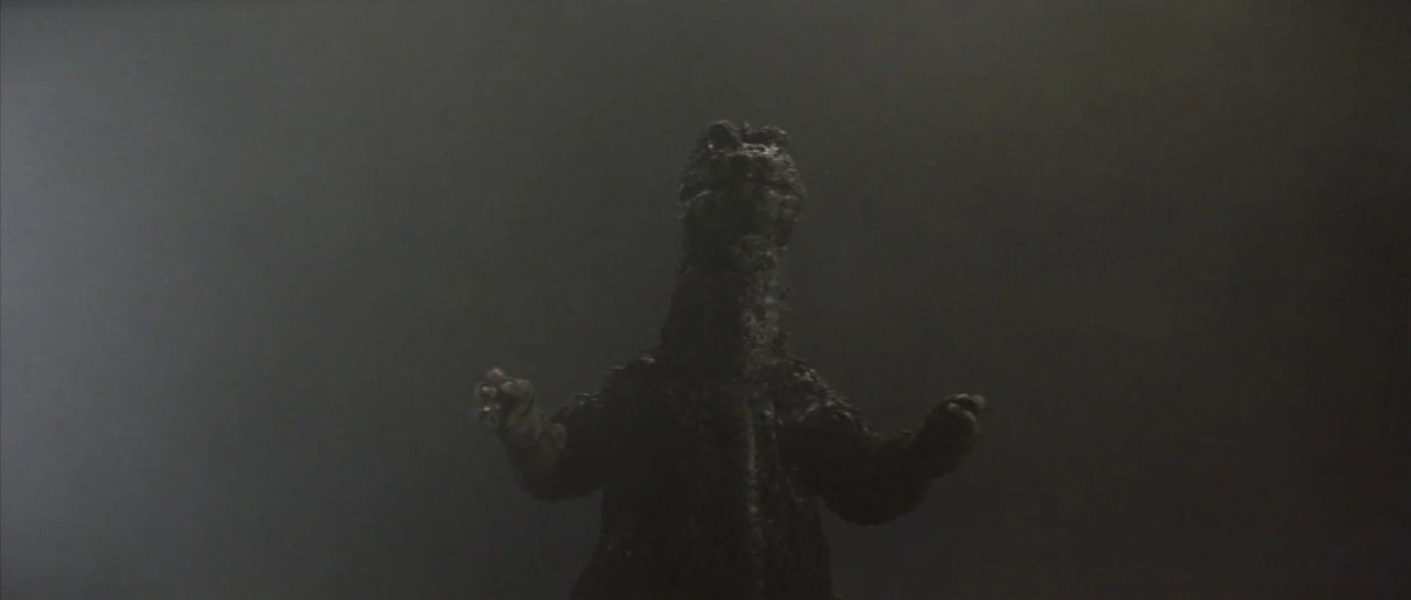 Godzilla Vs Hedorah (1971) movie still: medium — A dark, hazy environment filled with smoke or fog obscures the distant ground. A large reptilian…