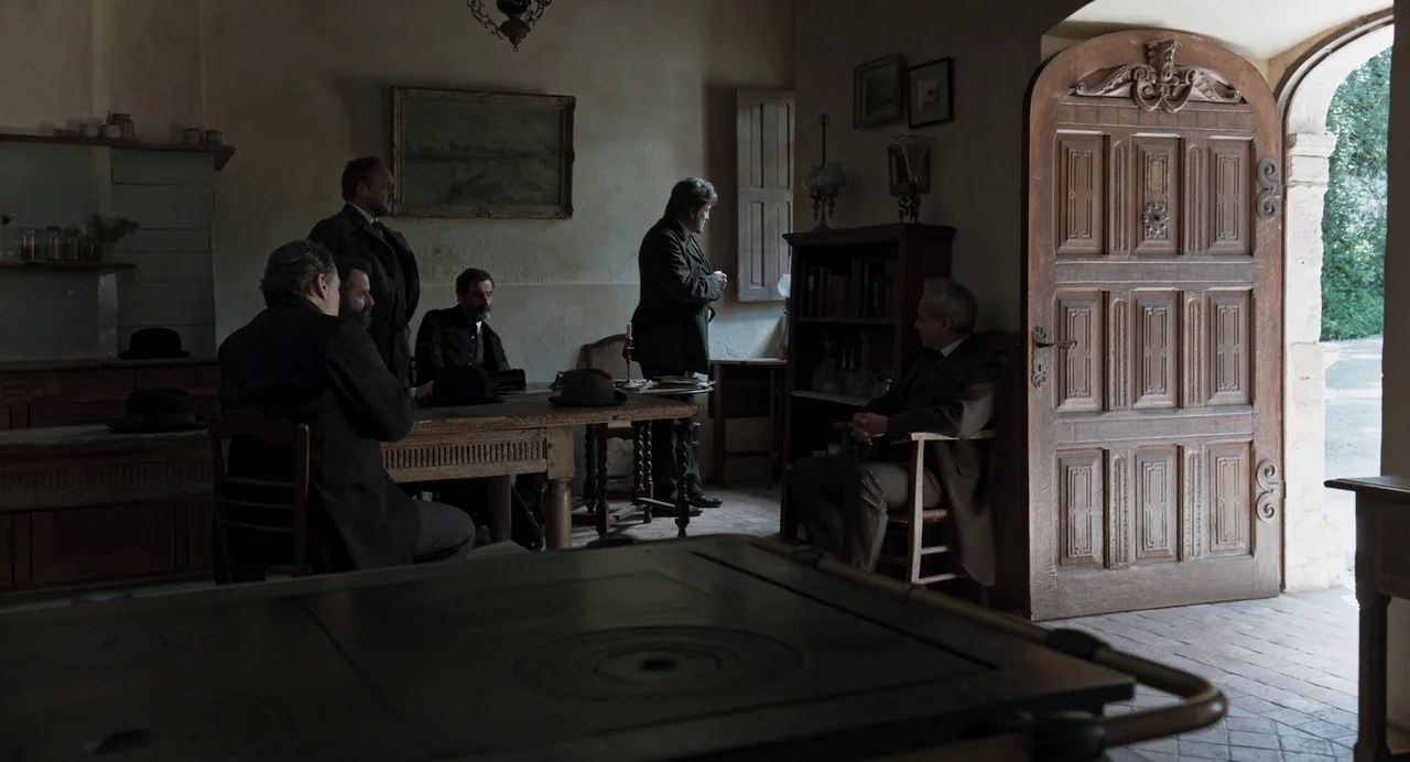 The Taste of Things (2023) movie still: wide — A 19th-century study with plaster walls, wooden furniture, and a large arched doorway. Five men in…
