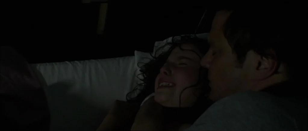 Genova (2008) movie still: closeup — A dark, dimly lit bedroom setting features a white pillow behind the subjects. An adult man and a young girl…