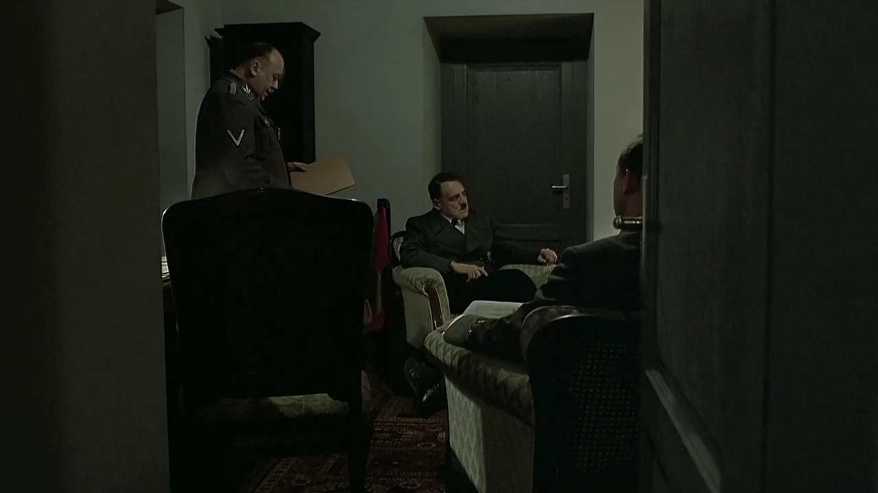 Downfall (2004) movie still: wide — An austere room with bare walls contains several armchairs and a small carpet. Three men in uniforms converse…
