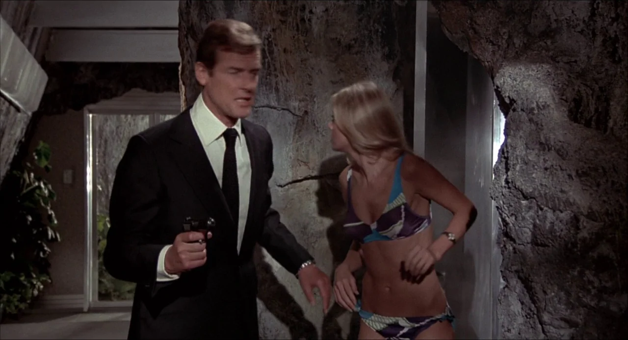 The Man With the Golden Gun (1974) movie still: medium — A man and a woman stand inside a cavernous structure with artificial rock walls. The man…