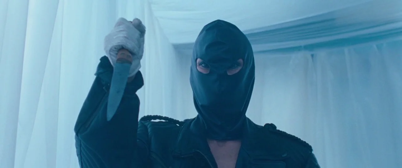 Knife+Heart (2018) movie still: medium — A person stands before floor-to-ceiling white fabric drapes in an enclosed space. The figure wears a…