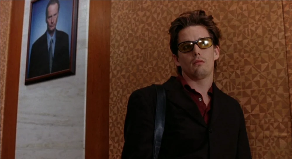 Hamlet (2000) movie still: medium — A man stands inside an elevator with geometric brown patterned walls. A framed portrait of a man in a suit hangs…