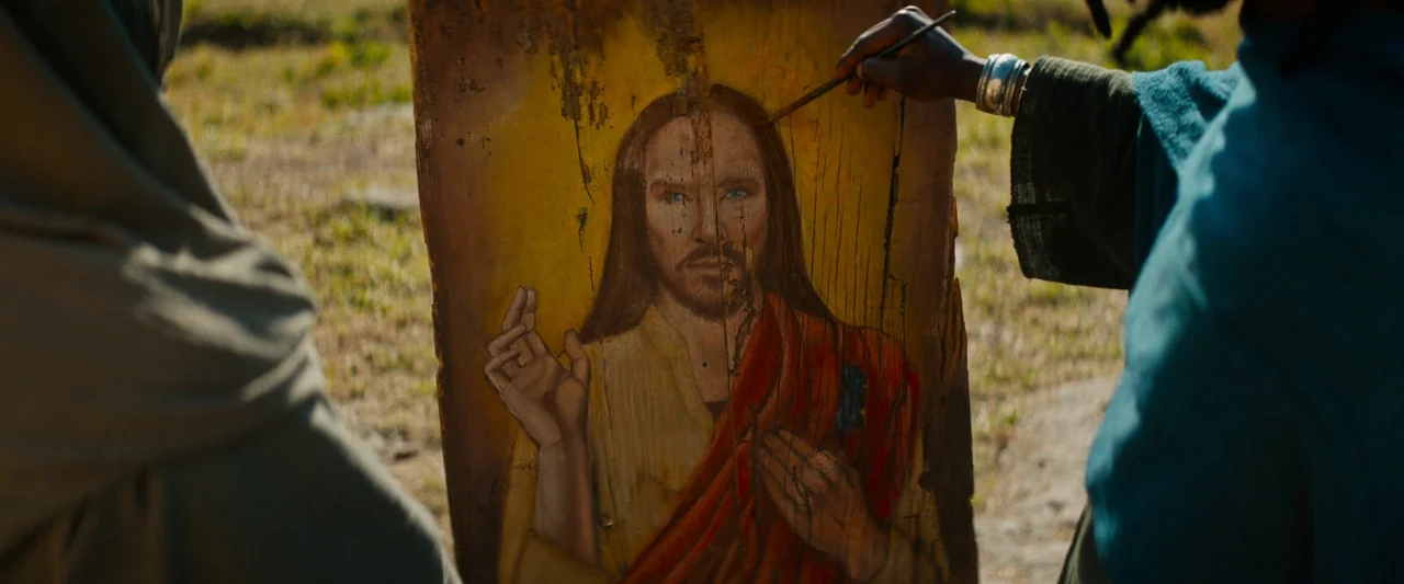 The Book of Clarence (2023) movie still: medium — A person uses a thin brush to apply pigment to a worn wooden panel. The subject is an icon…