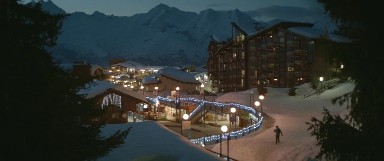 Force Majeure (2014) movie still: wide — A high-altitude ski resort village rests nestled against a large snow-covered mountain range. Many windows…