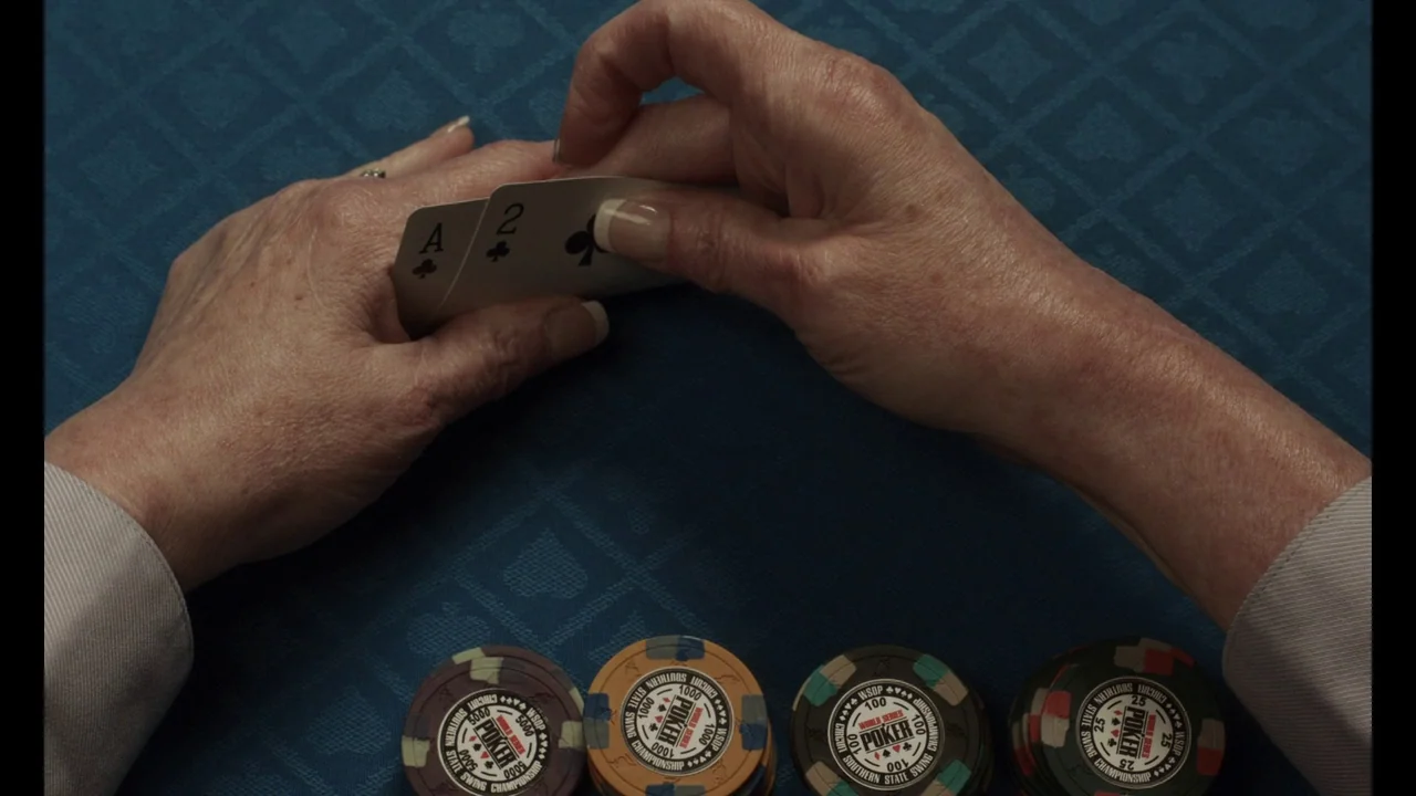 The Card Counter (2021) movie still: closeup — A blue felt poker table surface holds several stacks of numbered plastic chips. Two playing cards, an…