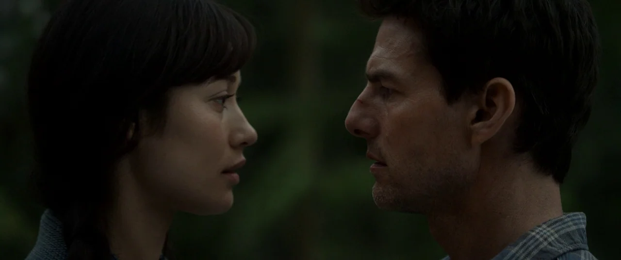 Oblivion (2013) movie still: closeup — Two individuals stand facing each other closely within a dimly lit, blurred outdoor setting. The woman and…