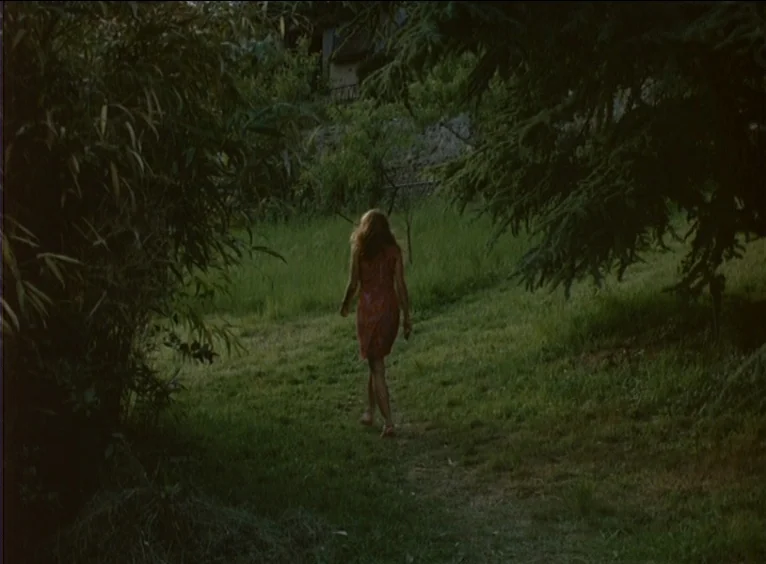 La Collectionneuse (1967) movie still: fullbody — A grassy clearing is framed by thick, dark green trees and dense bamboo foliage. A woman with long…