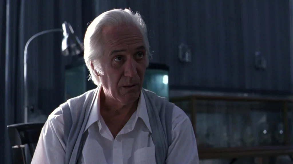 Cronos (1993) movie still: medium — A dimly lit room with dark paneling serves as the backdrop. An older man with silver hair sits in the foreground.