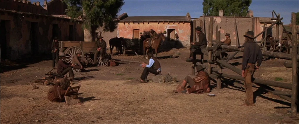 Pat Garrett & Billy The Kid (1973) movie still: wide — A dusty, sun-bleached courtyard is surrounded by dilapidated adobe buildings and wooden…