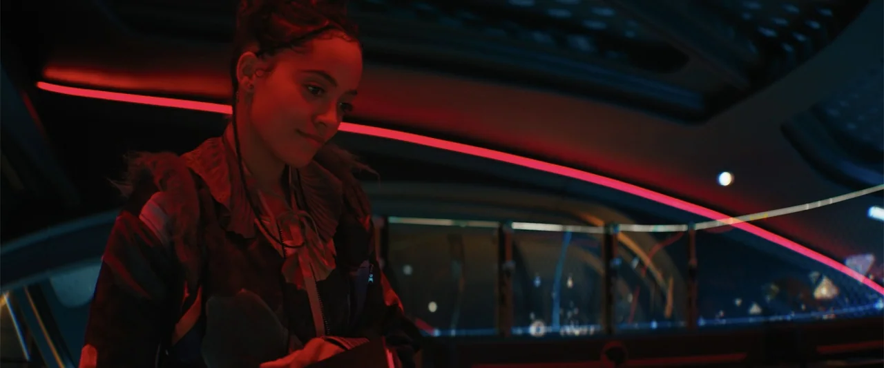 Black Adam (2022) movie still: medium — A dark, futuristic cockpit interior features curved panels and glowing red light strips. A young woman with…
