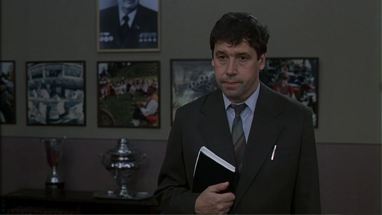 Citizen X (1995) movie still: medium — A dimly lit room features framed photographs and a metallic trophy on a shelf. A middle-aged man stands in…
