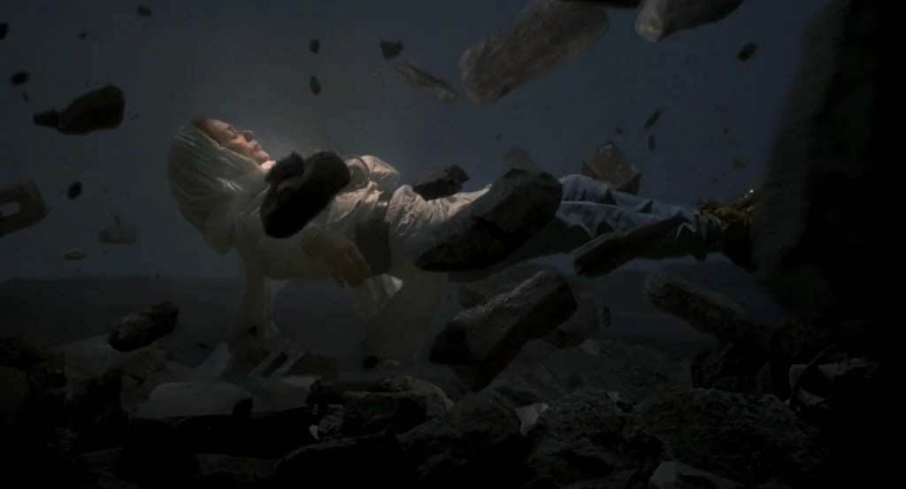 Louder Than Bombs (2015) movie still: medium — A dark, atmospheric space is filled with suspended rocks and fragments of rubble. A woman wearing a…