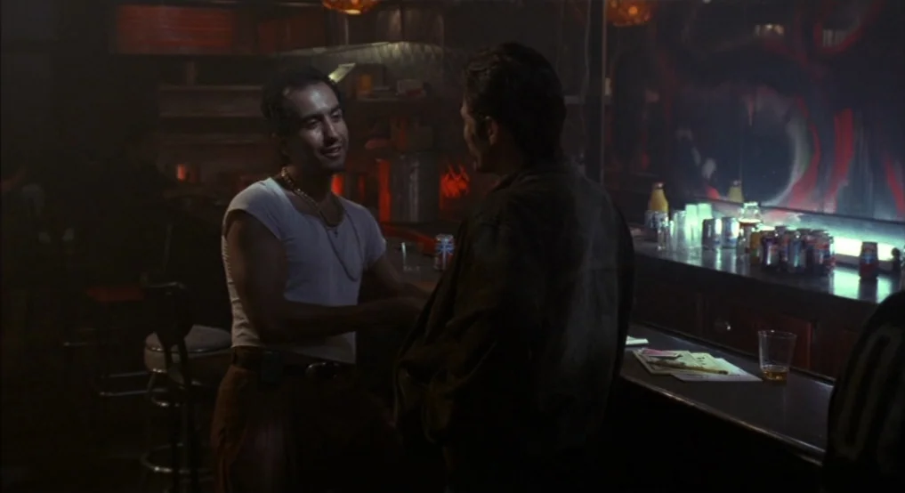 Light Sleeper (1992) movie still: medium — A dimly lit tavern with a wooden counter and shadowy seating areas in back. Two men stand together at the…