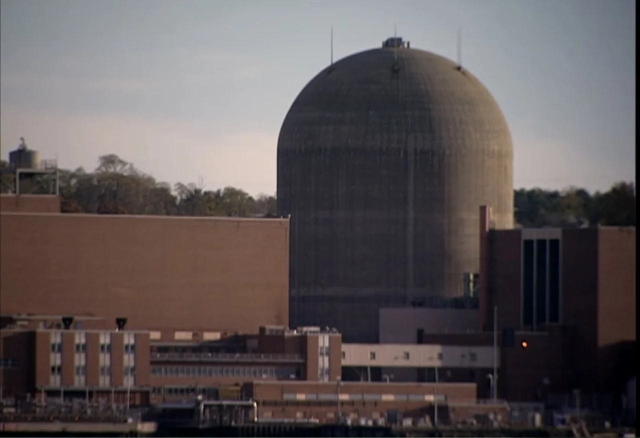 Indian Point: Imagining the Unimaginable (2004) movie still: establishing — A large concrete nuclear containment dome rises above a complex of brown…