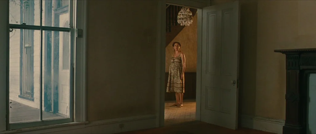 Away We Go (2009) movie still: wide — A rustic house interior featuring a tall window on the left and an open door. A pregnant woman stands in the…