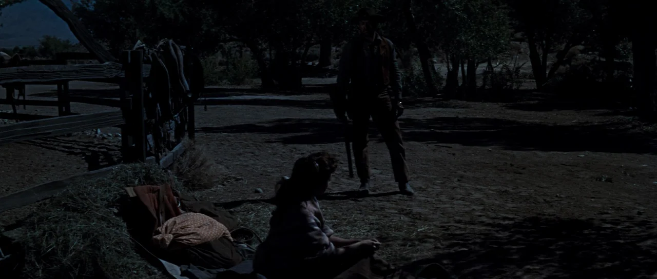 Comanche Station (1960) movie still: fullbody — A dark, moonlit outdoor area features a wooden fence with saddles hanging on it. A cowboy stands…