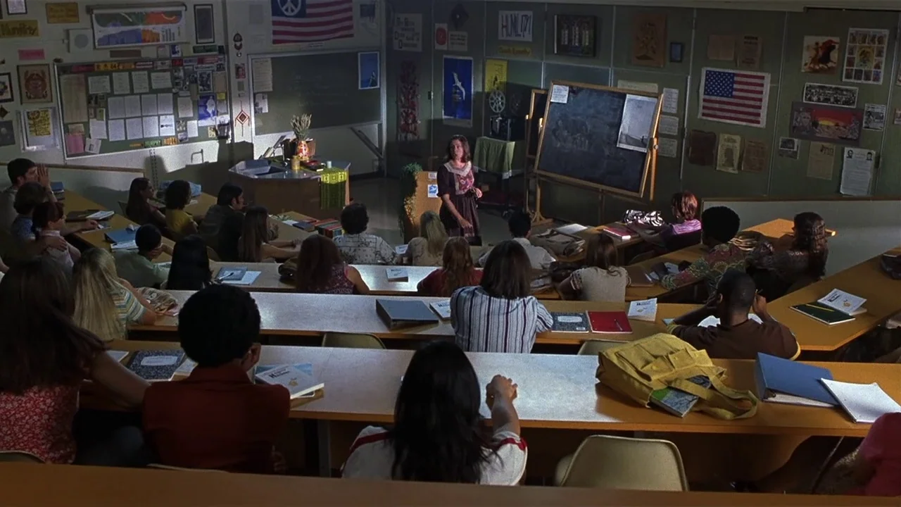 Almost Famous (2000) movie still: wide — A tiered classroom features walls covered with educational posters and American flags. A teacher presents…