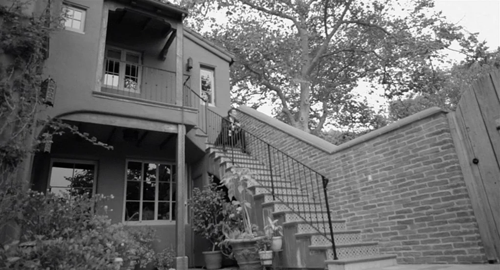 Much Ado About Nothing (2012) movie still: wide — A two-story residential building features a stucco exterior and a stone staircase. A metal railing…