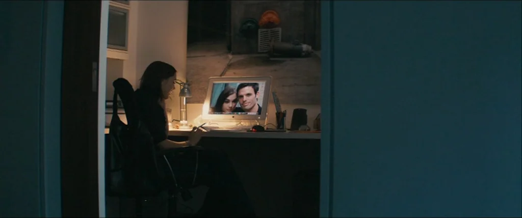 The Girlfriend Experience (2009) movie still: wide — A woman sits in a dark room illuminated by the glow of a computer. She looks at a screen…